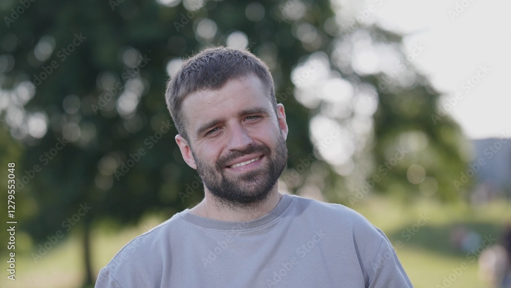 A cheerful young man stands outdoors, enjoying the natural surroundings with a tree in the background. A cheerful young man stands outdoors, enjoying the natural surroundings with a tree in the background.