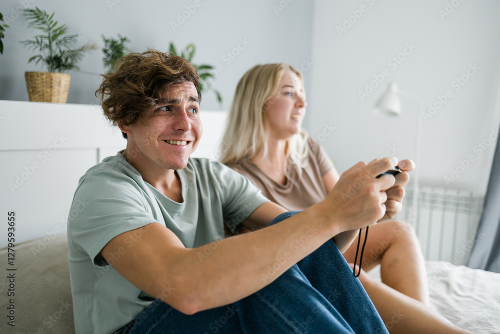 Young couple in love playing video games while lying on the bed in the bedroom, having fun and enjoying each other on their weekends. Technologies and gaming concept Young couple in love playing video games while lying on the bed in the bedroom, having fun and enjoying each other on their weekends. Technologies and gaming concept