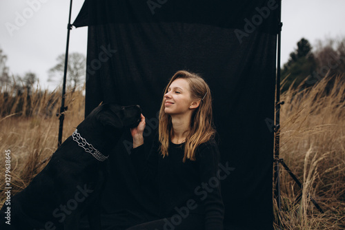 beautiful woman dressed in black pants and  sweater sits on a black background with a beautiful black Labrador dog.  Labrador Retriever dog