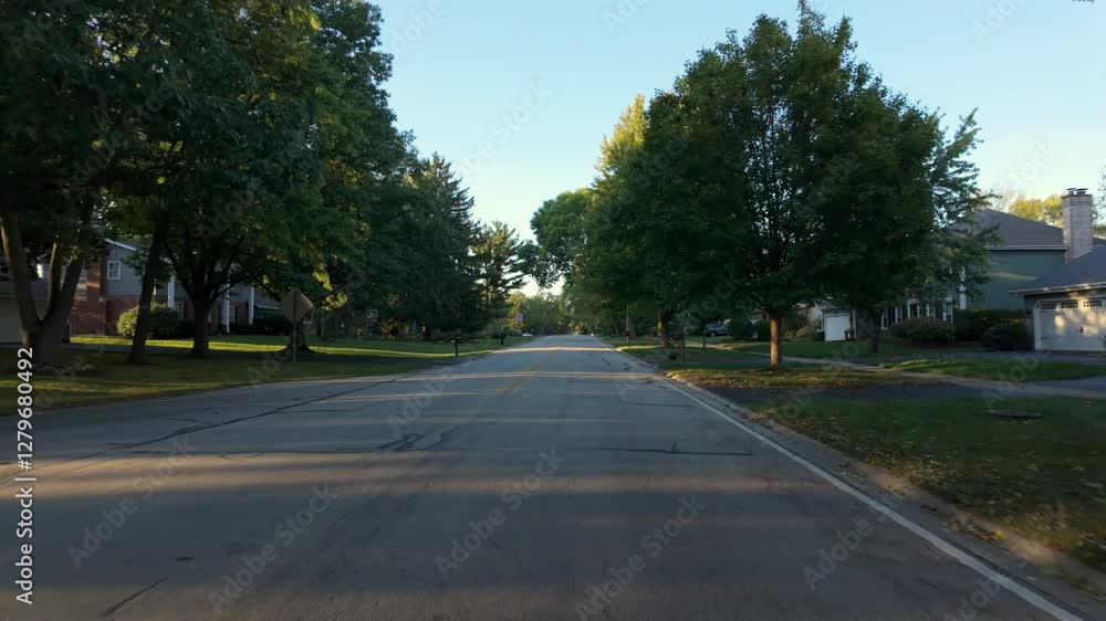 A wide POV shot of neighborhood green street in a U.S. residential suburbs on a beautiful sunny day, filmed from a moving car. A wide POV shot of neighborhood green street in a U.S. residential suburbs on a beautiful sunny day, filmed from a moving car.