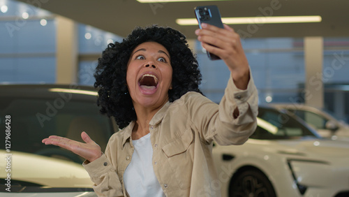Joyful girl African American woman blogger taking selfie photo in car showroom buying new auto in dealership salon happy cheerful client buyer blogging with smartphone advertising automobile vehicle