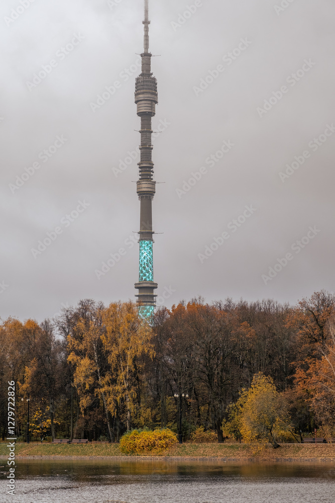 Obraz premium Tower surrounded by autumn trees near the water in a cloudy setting showcasing illumination in the evening sky