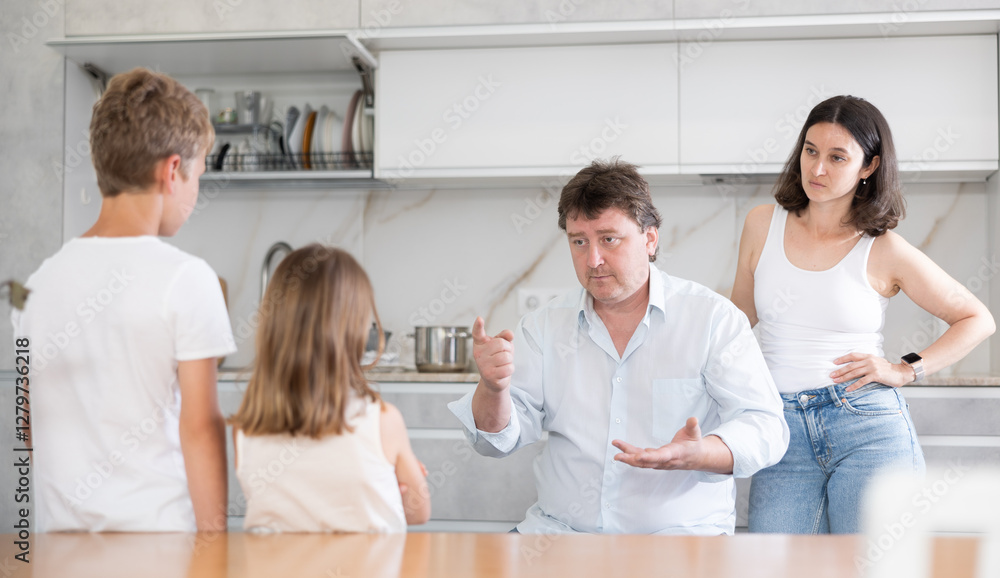 Fototapeta premium Mom and dad scold their guilty daughter and son in kitchen at home
