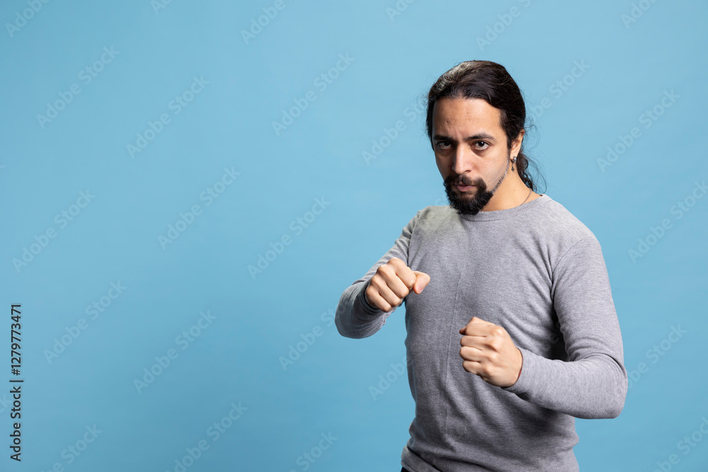 Aggressive strong person clenching fists and preparing to fight against blue background, showing his strength and determination for a physical challenge. Man prepares for confrontation, fist up. Aggressive strong person clenching fists and preparing to fight against blue background, showing his strength and determination for a physical challenge. Man prepares for confrontation, fist up.