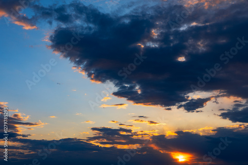 Dramatic sunset cloudscapes, showcasing a vibrant mix of colors and textures. Golden hour hues paint the sky as sun dips below the horizon. Dark and light clouds, highlighting the beauty of a sunset