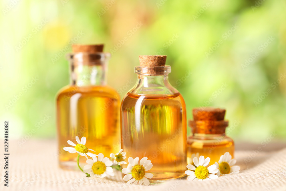 Bottles of essential oil and chamomile flowers on cloth, closeup Bottles of essential oil and chamomile flowers on cloth, closeup