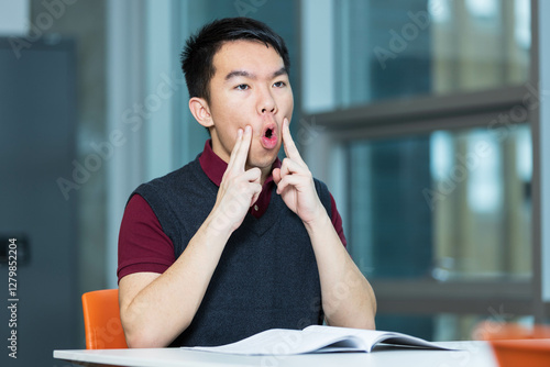 A young teenage boy is doing oral motor exercises in a room. He could be doing singing practice, vocal training, or speech therapy, improving articulation, enunciation and reducing speech impediments