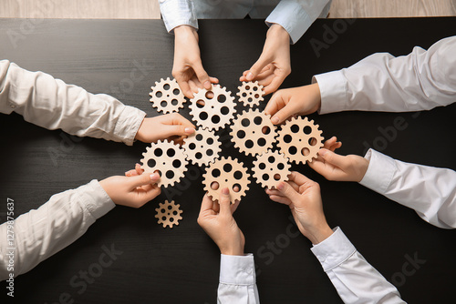 Hands holding wooden gears on dark wooden background, top view