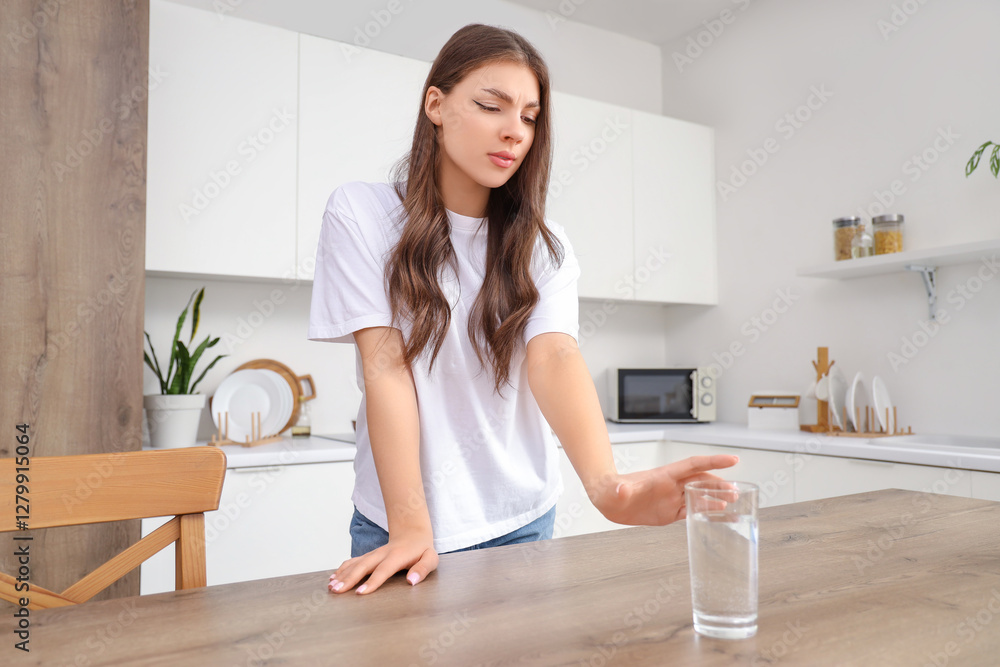 Young woman with panic attack taking glass of water from table in kitchen Young woman with panic attack taking glass of water from table in kitchen
