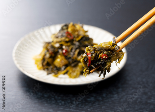 Lifting Karashi Takana with Chopsticks on a Black Background – Karashi Takana: A Japanese-Style Pickle Made from Mustard Greens