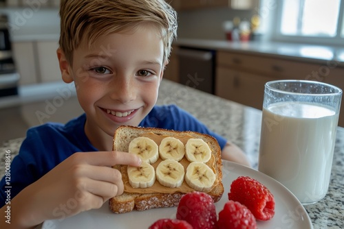 A boy takes a bite of a whole grain toast topped with peanut butter and banana slices. The breakfast table is set with milk