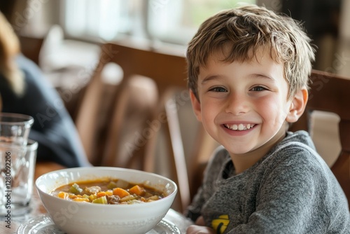 A young boy smiles as he eats a bowl of homemade vegetable soup
