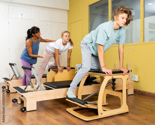 Teen boy and girl in sportswear keeps the balance, pilates training on exercise machine in gym. Fitness workuot in sport club photo