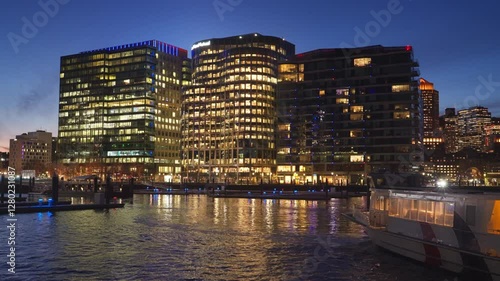 View of public boat coming into the pier at Seaport District in Boston, MA during evening sunset in winter with commercial buildings in background