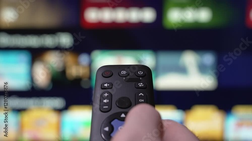 Person Browsing Streaming Services Using Remote Control. Hand Holding a Remote Control Browses Various Streaming Services On a Large Screen. Focused on the Hand. Turn Off smart TV. Internet TV