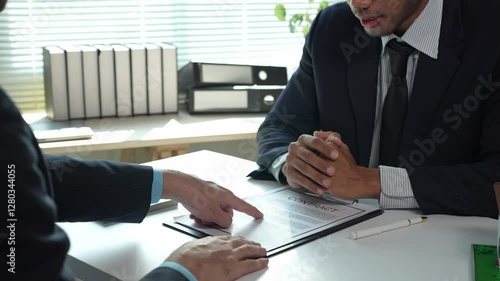 Business partners discussing terms of contract, pointing at specific clauses, gesturing, and finally shaking hands after reaching an agreement in a bright office environment