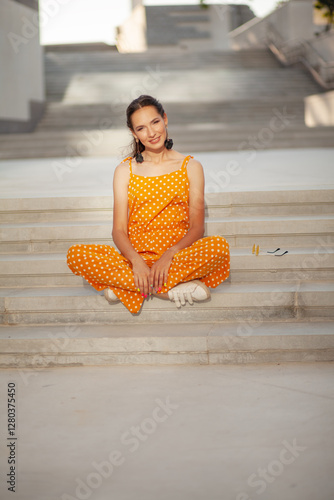 a beautiful girl in a bright clothes walks around the city in the summer. Young womn smiling against the biege wall and sun kight photo