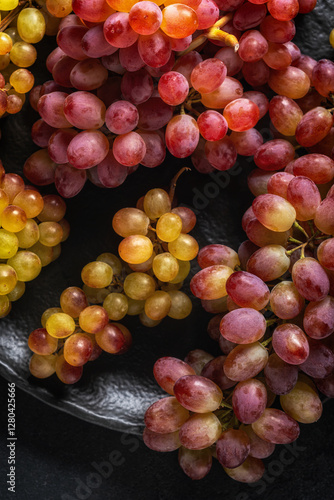 Close-up of red and yellow grapes on a dark textured plate with soft lighting and a dark background