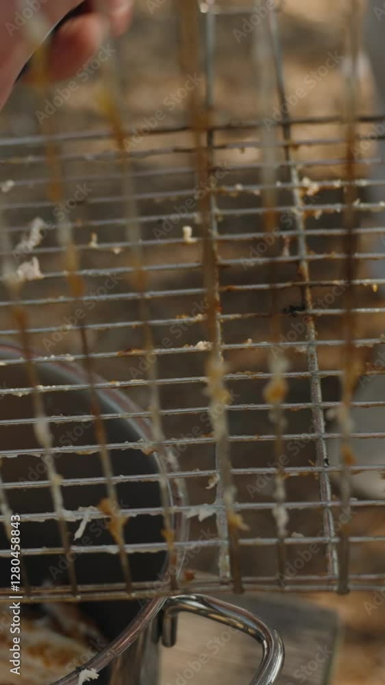 Vertical video. Piece Of Meat Stuck To The Grill Rack Being Pulled Off With Tongs, While Grilled Meat Collects In A Metal Pot Below In An Outdoor Setting Vertical video. Piece Of Meat Stuck To The Grill Rack Being Pulled Off With Tongs, While Grilled Meat Collects In A Metal Pot Below In An Outdoor Setting