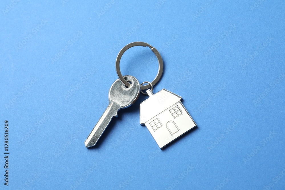 Metallic key with keychain in shape of house on color background Metallic key with keychain in shape of house on color background