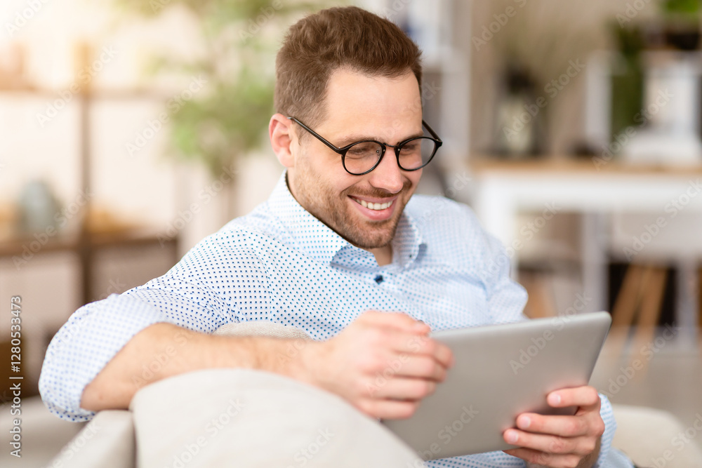 Reading News. Smiling man in spectacles using digital tablet sitting on the couch, copyspace Reading News. Smiling man in spectacles using digital tablet sitting on the couch, copyspace