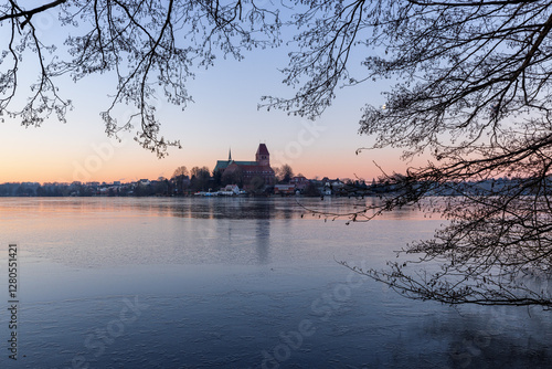 Doem of Ratzeburg at a beautiful winter morning with ice covered lake, framed by branches and twigs, Schleswig-Holstein, Northern Germany