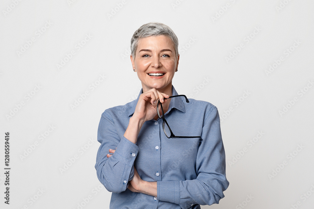 Portrait Of Beautiful Mature Businesswoman Holding Glasses And Smiling At Camera While Posing On Light Background In Studio, Free Space Portrait Of Beautiful Mature Businesswoman Holding Glasses And Smiling At Camera While Posing On Light Background In Studio, Free Space
