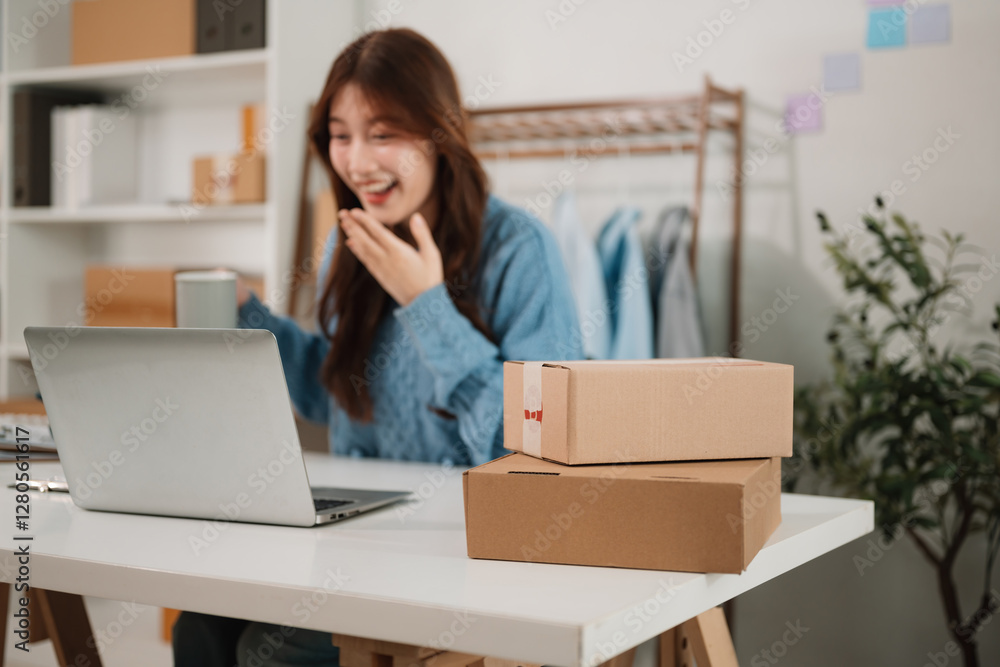 A focus on parcel boxes on workbench against A young entrepreneur reacts with excitement while working on her laptop, Celebrating a business achievement, Rewarding journey of running an online store A focus on parcel boxes on workbench against A young entrepreneur reacts with excitement while working on her laptop, Celebrating a business achievement, Rewarding journey of running an online store