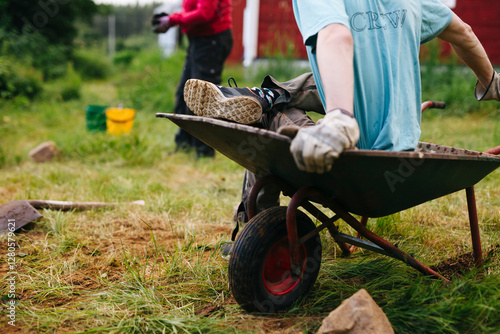 Low section of boy wearing gardening gloves and sitting on wheelbarrow photo