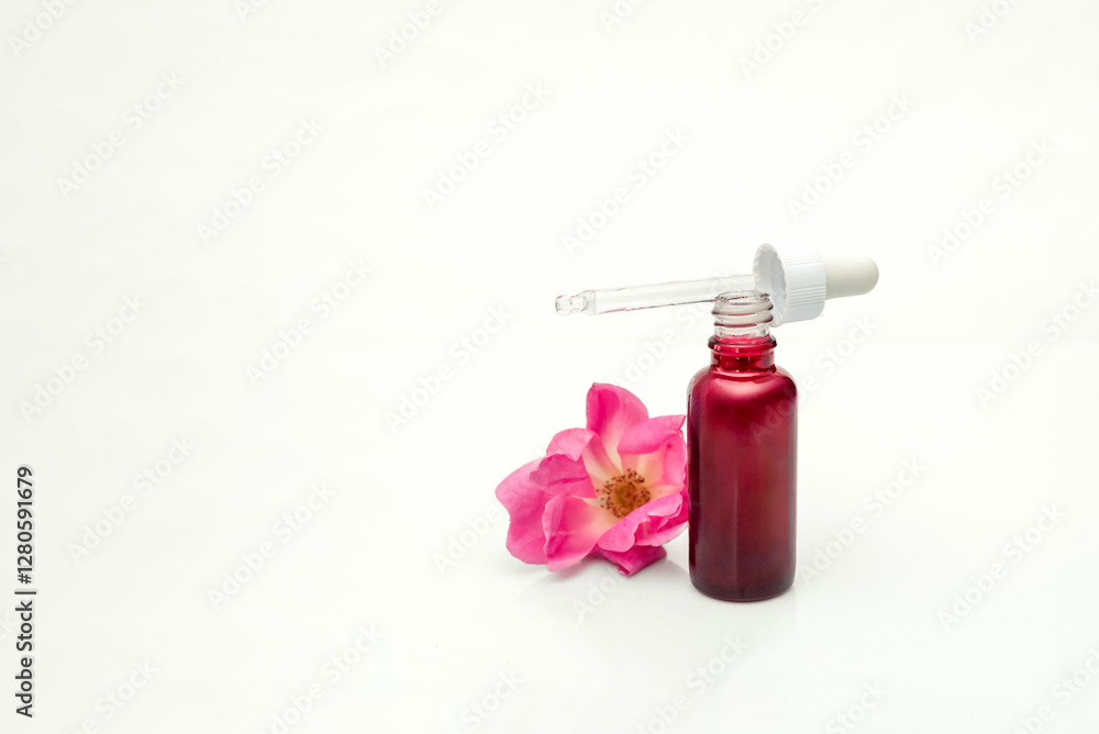 Rose essential oil dripping from dropper into bottle for skincare treatment on white background Rose essential oil dripping from dropper into bottle for skincare treatment on white background