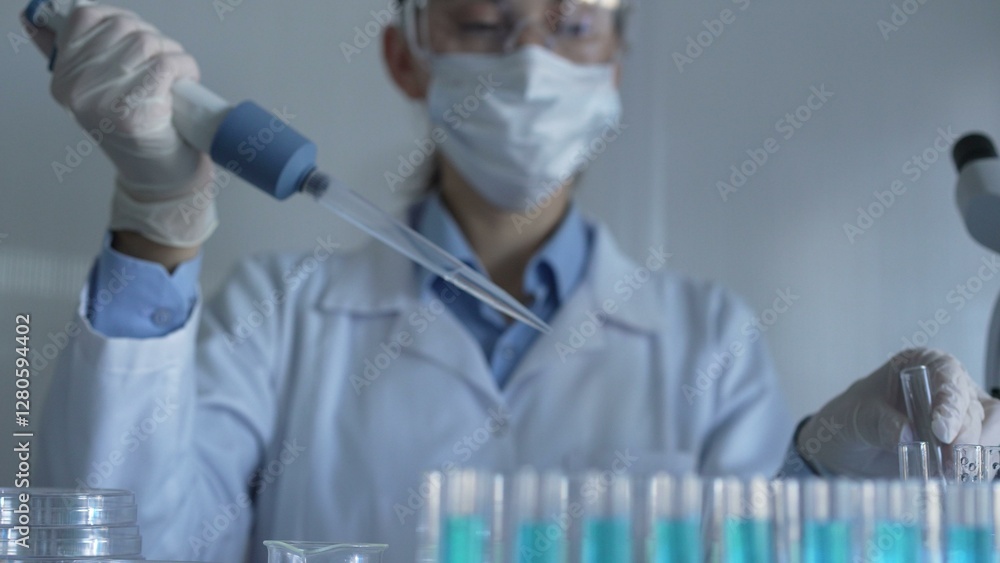 Scientist woman, wearing a lab coat, mask, blue gloves and safety glasses, is using a micropipette to drop a liquid into a test tubes. Medicine and science Scientist woman, wearing a lab coat, mask, blue gloves and safety glasses, is using a micropipette to drop a liquid into a test tubes. Medicine and science