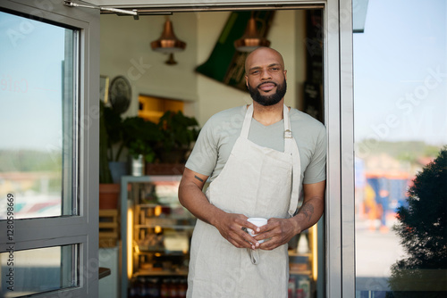 Portrait of male owner holding coffee mug and leaning on cafe doorway