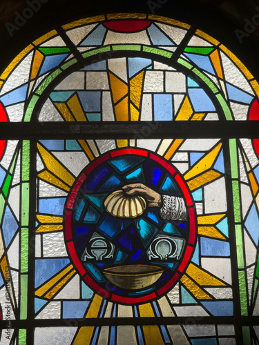 Colorful stained glass depicting a hand holding a shell above chalices and a bowl.