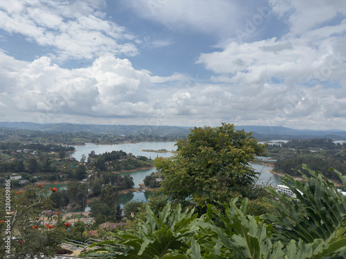 Scenic view of a serene lake surrounded by lush greenery and distant hills under a cloudy sky.