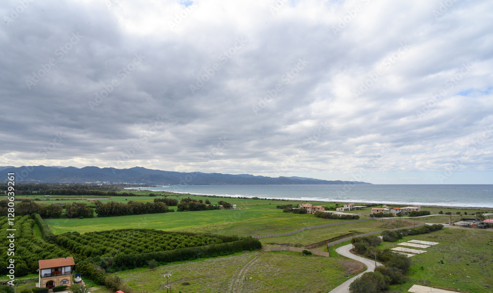 Obraz premium Breathtaking coastal landscape with lush farmland and distant mountains near the serene sea