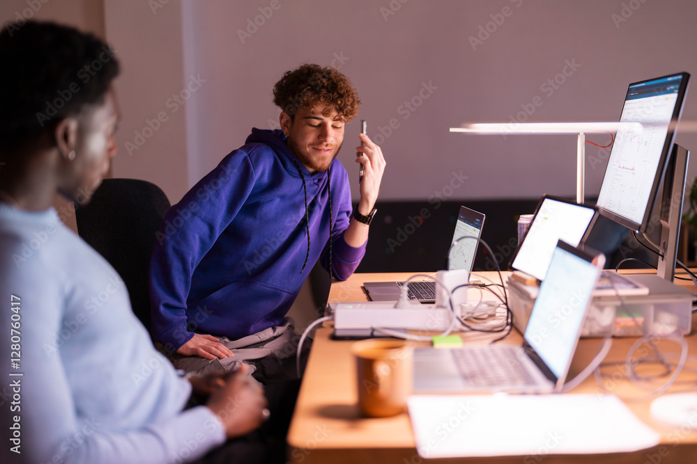 Two young professionals sit at a shared desk, reviewing financial charts and stock market trends on multiple monitors in a dimly lit office setting. Two young professionals sit at a shared desk, reviewing financial charts and stock market trends on multiple monitors in a dimly lit office setting.