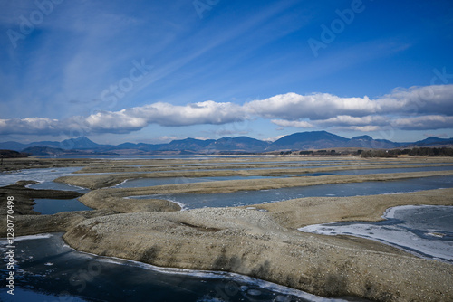 A picturesque view of the drying bottom of Liptovská Mara with exposed sandy areas, remnants of ice and mountains in the background under a cloudy sky photo