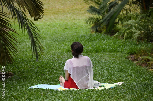 Picture of a woman sitting on the grass and meditating in a park enjoying the peace and nature. lifestyle background.