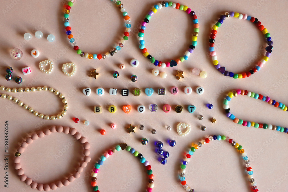 Friendship bracelet spelled with letter beads. Colorful handmade bracelets and various beads. Flat lay, pink background.