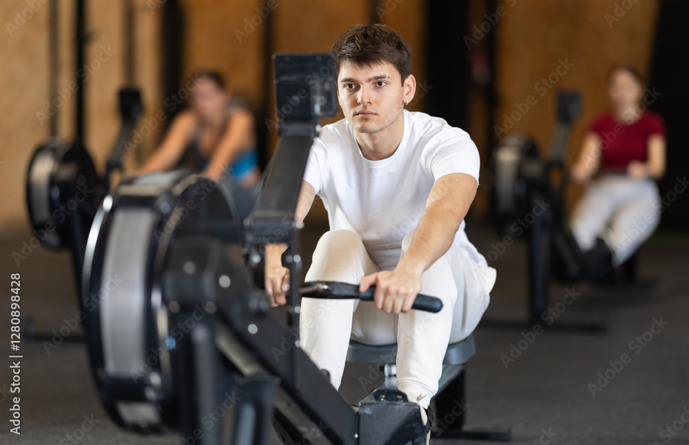 Guy exercises on a rowing machine in the gym. European man is preparing for the rowing competition. Fitness club client at a group cardio workout