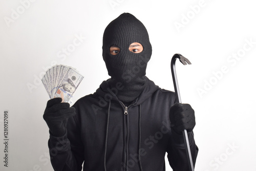 Thief wearing black jacket and mask holding crowbar, showing dollar bills isolated on white background. Robbery and crime concept photo