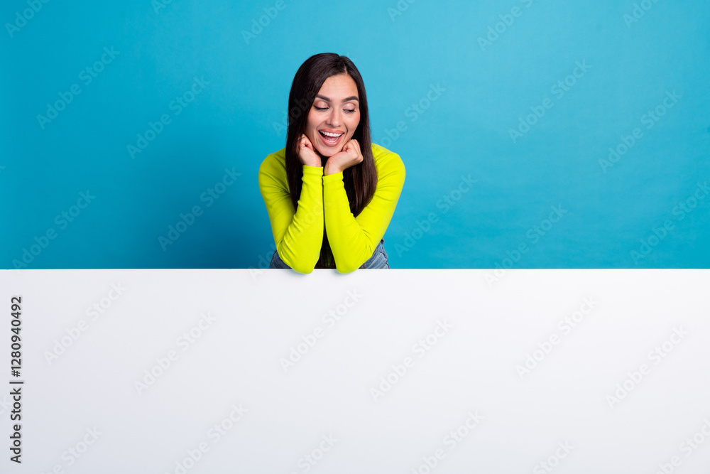 Smiling young woman in yellow long sleeve top posing on a table against a blue background for a trendy and cheerful advertising concept Smiling young woman in yellow long sleeve top posing on a table against a blue background for a trendy and cheerful advertising concept
