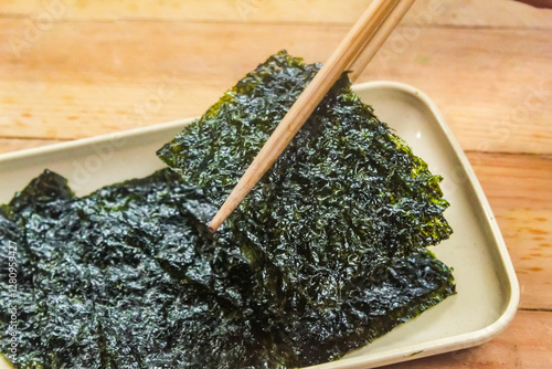 chopsticks picking up nori seaweed in a plate on a wooden table