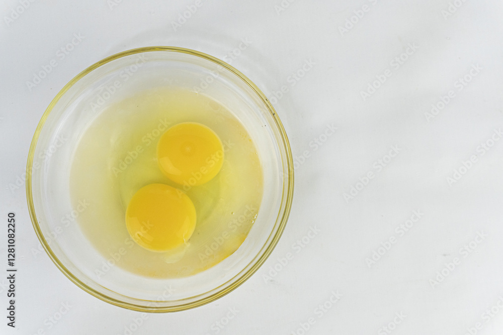 Two raw egg yolks in a glass bowl on a white surface, ideal for food photography and culinary applications. Two raw egg yolks in a glass bowl on a white surface, ideal for food photography and culinary applications.