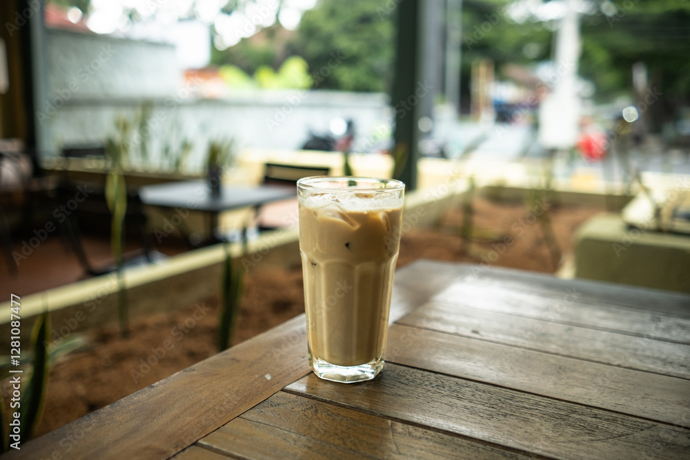 An iced café latte placed on a table with a blurred background of multiple tables in an outdoor setting, creating a relaxed café atmosphere An iced café latte placed on a table with a blurred background of multiple tables in an outdoor setting, creating a relaxed café atmosphere
