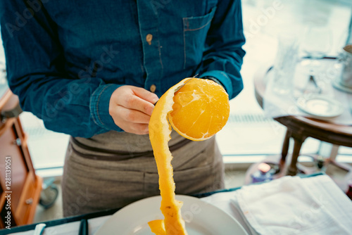 Waiter performing an elegant table service demonstration with a knife and fork on an orange. Fine dining etiquette and professional restaurant service photo