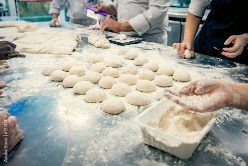Hands of baking students working with fresh dough in a professional kitchen. Artisan bread preparation, teamwork, and pastry training in a culinary school. Flour, dough balls, and rolling techniques.