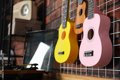 Three colorful ukulele on brick wall and record player indoors, closeup