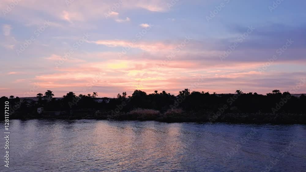 A stunning sunset over the Nile River, featuring a sky painted in pink, orange, and blue hues. Silhouettes of palm trees line the riverbank, reflecting beautifully in the water. Egypt. A stunning sunset over the Nile River, featuring a sky painted in pink, orange, and blue hues. Silhouettes of palm trees line the riverbank, reflecting beautifully in the water. Egypt.
