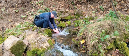 A man with a camera washes his hands in a stream near a spring on an autumn day